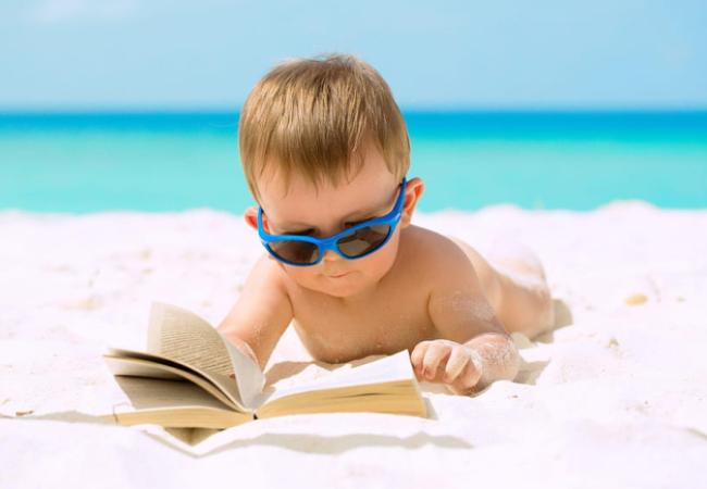Young boy on the beach reading a book
