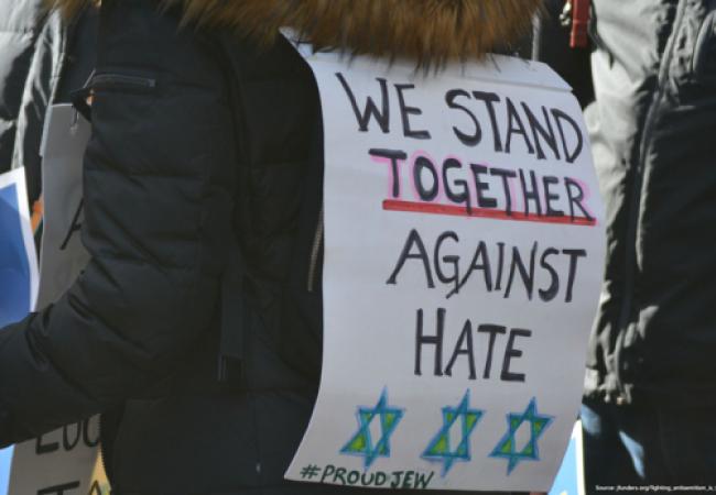 Person in a crowd wearing a placard that says "We stand together against hate"