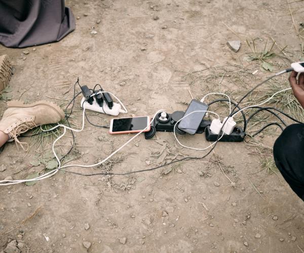 Cell phones with charger cables plugged into power bars on the ground outdoors