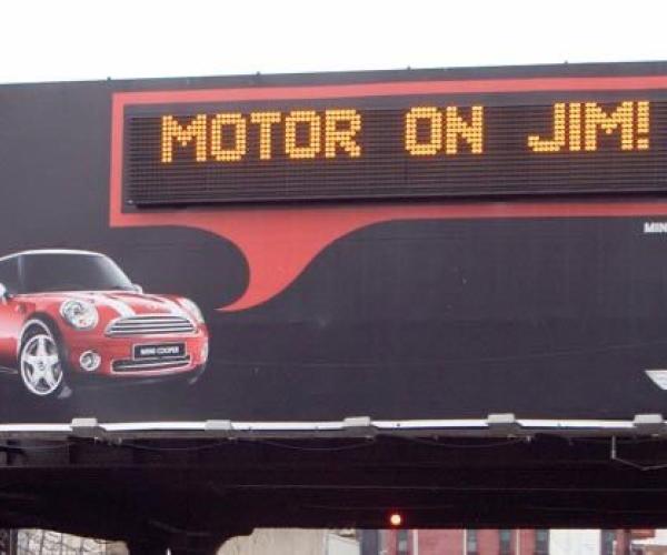 Mini Cooper billboard displaying a personalized message that says, "Motor on Jim!"
