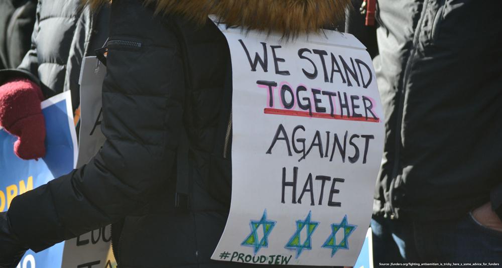 Person in a crowd wearing a placard that says "We stand together against hate"