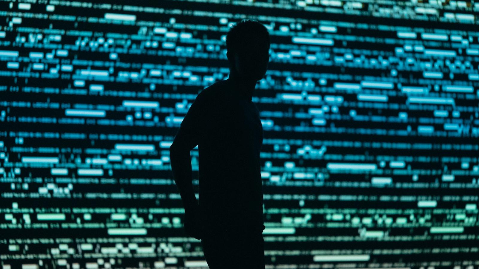 Surveillance, illustrated by the silhouette of a man in front of a data wall