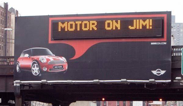 Mini Cooper billboard displaying a personalized message that says, "Motor on Jim!"