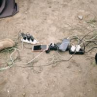 Cell phones with charger cables plugged into power bars on the ground outdoors